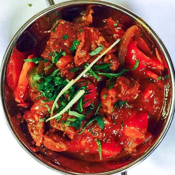 Indian curry with meat, red peppers, and onions, garnished with fresh cilantro and ginger.