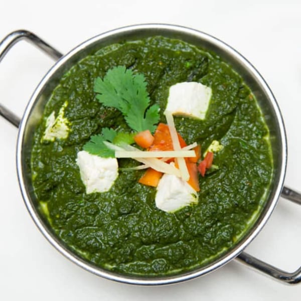 Palak Paneer, a vibrant green Indian spinach and cheese dish, garnished with cilantro, tomatoes, and ginger.