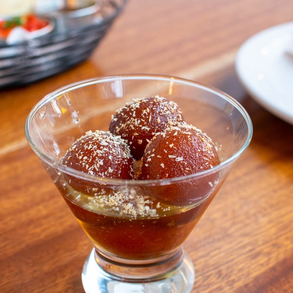 Three gulab jamun, Indian fried dough balls, in syrup and topped with coconut flakes, in a glass.