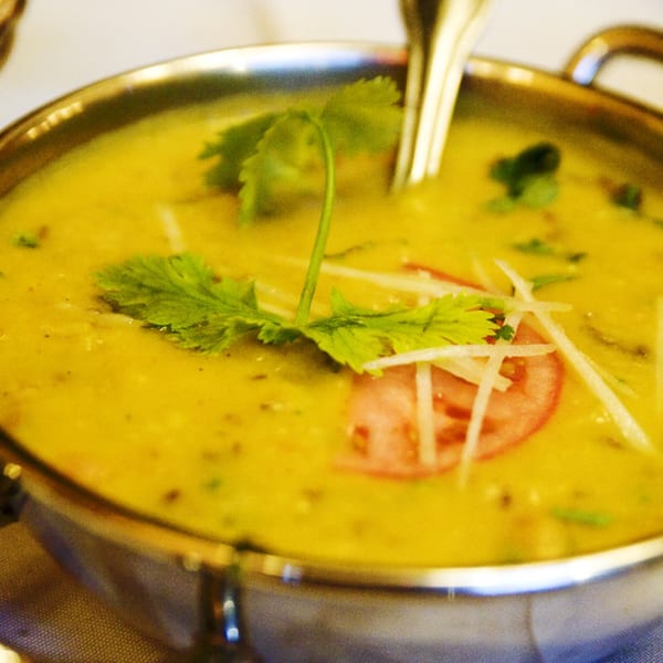 A golden Indian lentil dal, garnished with fresh cilantro, ginger slivers, and a tomato slice.