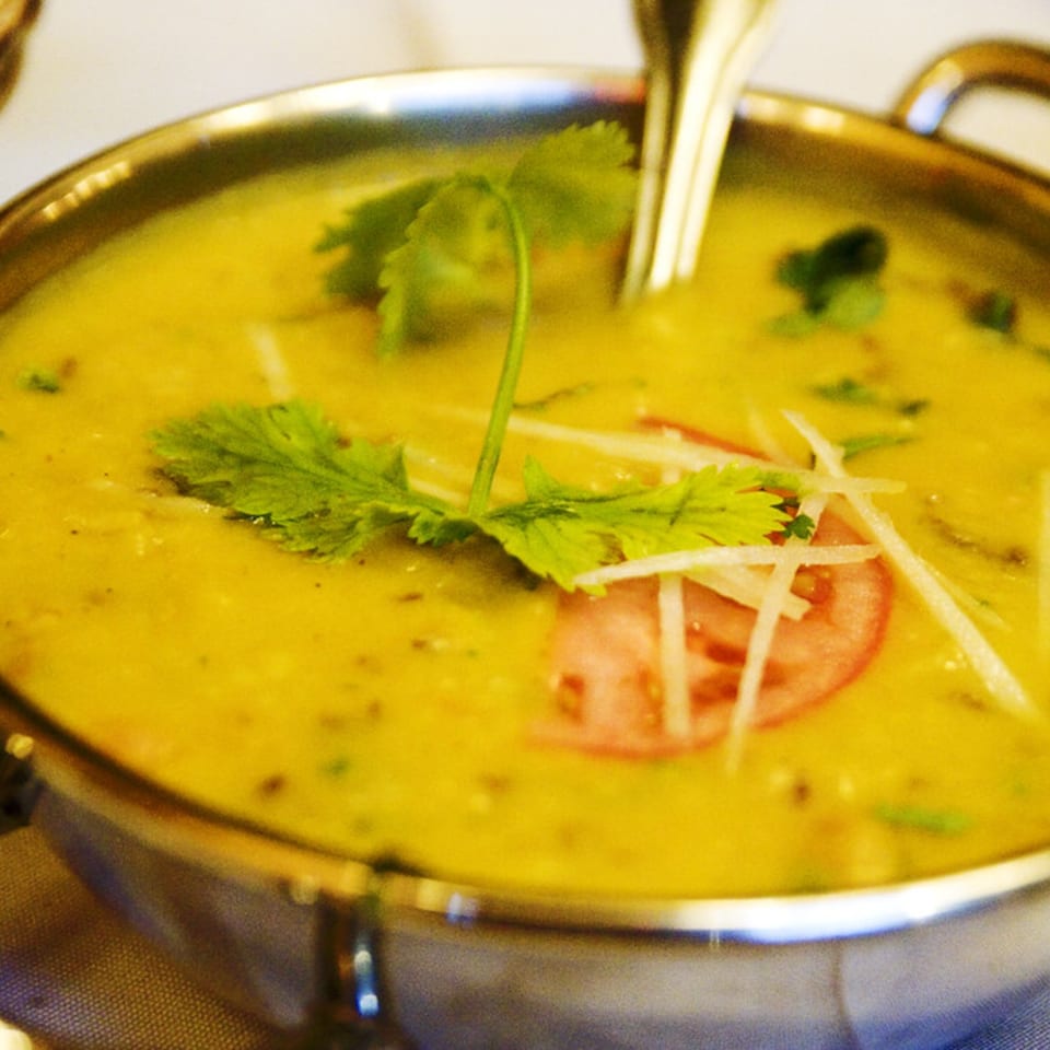 A golden Indian lentil dal, garnished with fresh cilantro, ginger slivers, and a tomato slice.