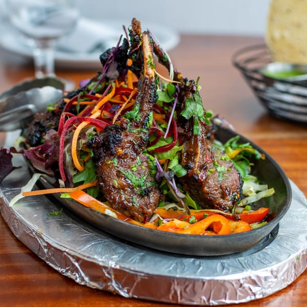 Indian lamb chops with fresh salad and vegetables in a cast iron pan on a wooden table.