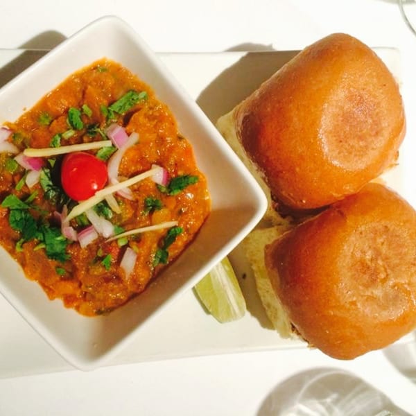 Pav Bhaji, a vibrant Indian vegetable curry, served with two soft bread rolls and a lime wedge.