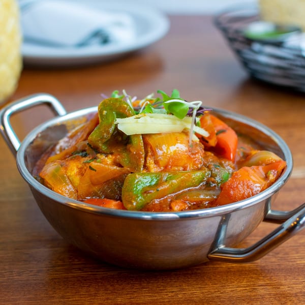 Indian Kadai Chicken with bell peppers and ginger in a metal serving bowl on a wooden table.